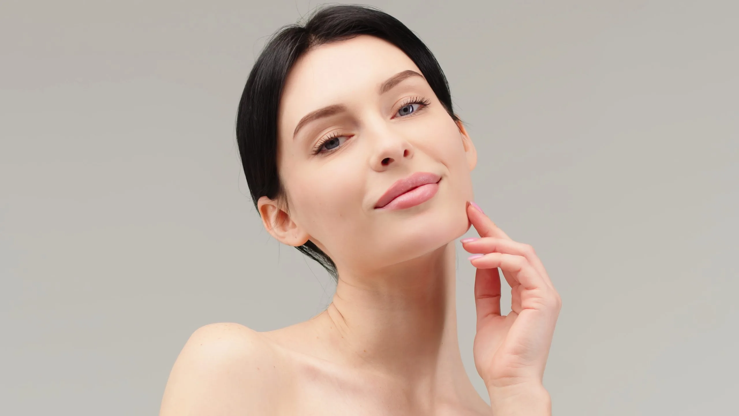 Woman touching her cheek and smiling against neutral gray background