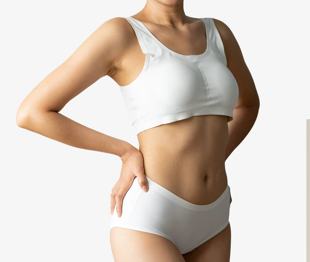 Woman in white sports bra and underwear examining her torso after body contouring