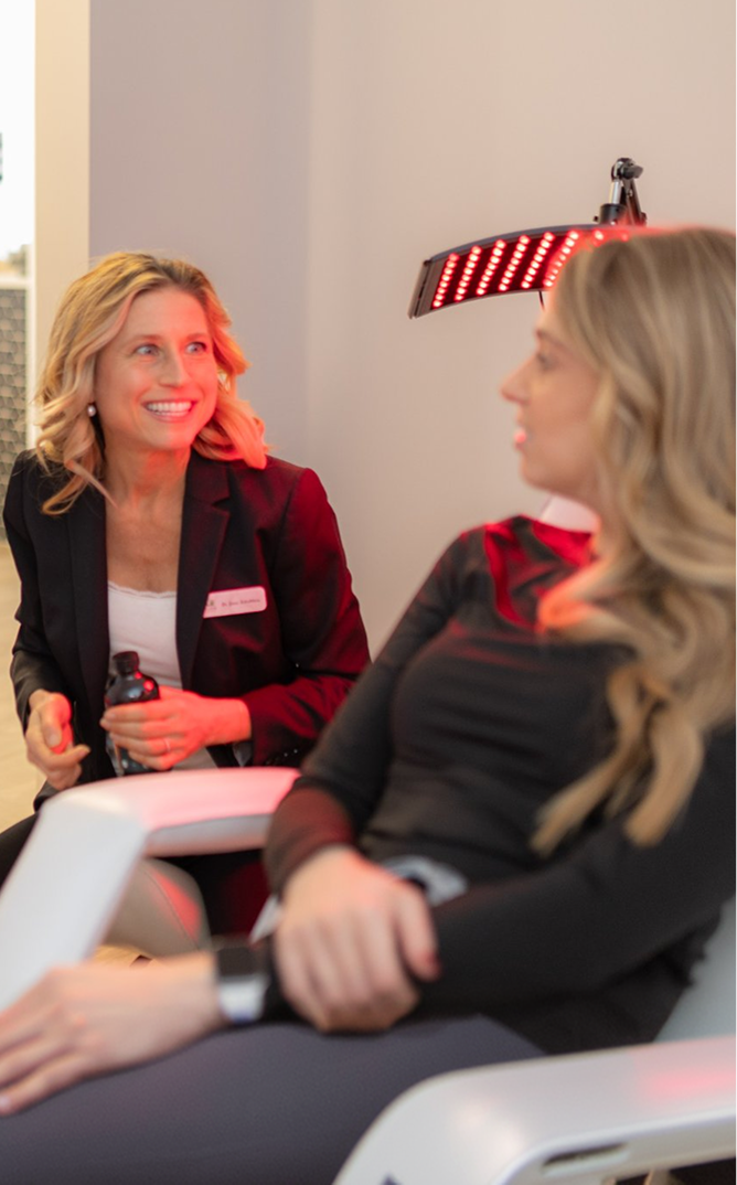 Dental professional in burgundy blazer consulting with patient under red therapeutic light during smile makeover consultation