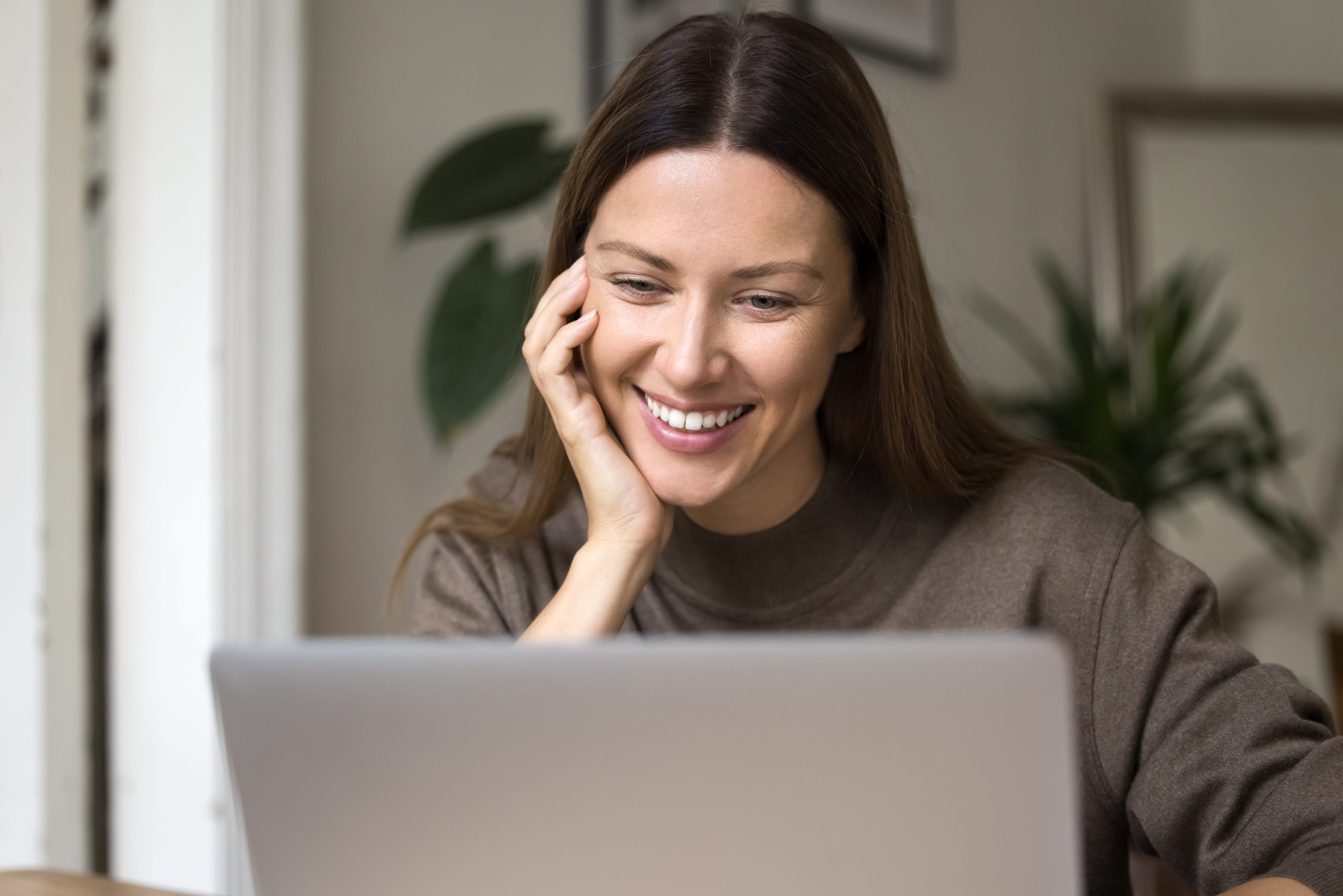 Woman smiling while using a laptop in a bright office with potted plants