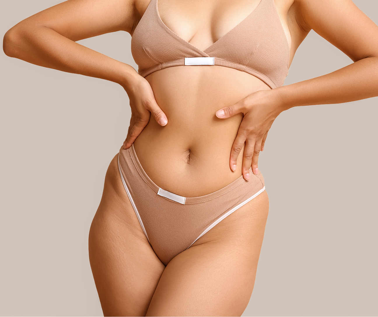 Woman in beige bikini examining her abdomen and sides with both hands