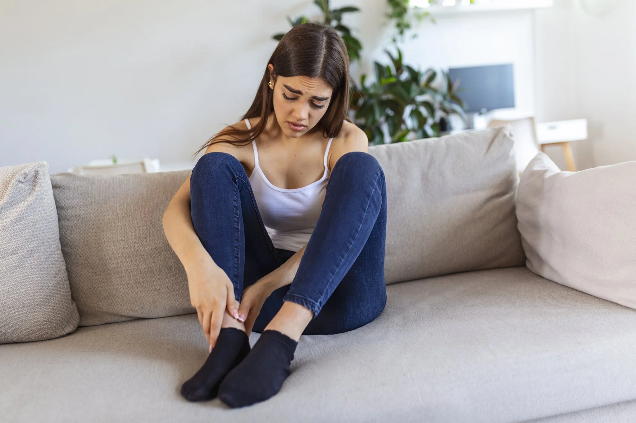 Woman sitting on a sofa holding a painful heel, illustrating why a heel may feel bruised