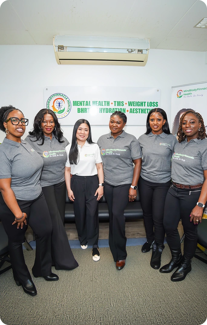 MindBodyPinnacle Health team of six members standing together in office with practice logo and service offerings displayed on wall behind them