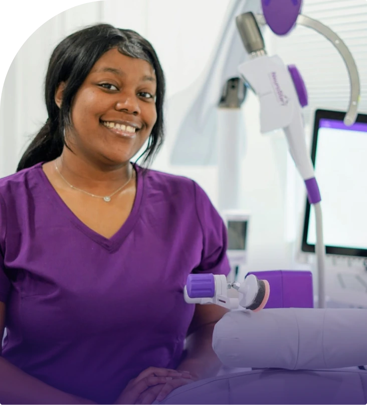 Team member in purple scrubs smiling at the practice's clinical equipment