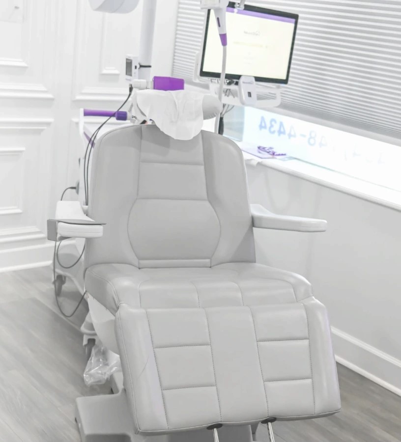 TMS therapy device with purple accents mounted above patient treatment chair in bright clinical room