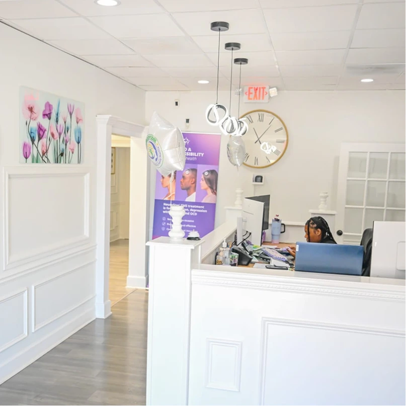 Reception area at MindBodySoul's Decatur office with staff member at front desk, floral artwork, and purple informational banner