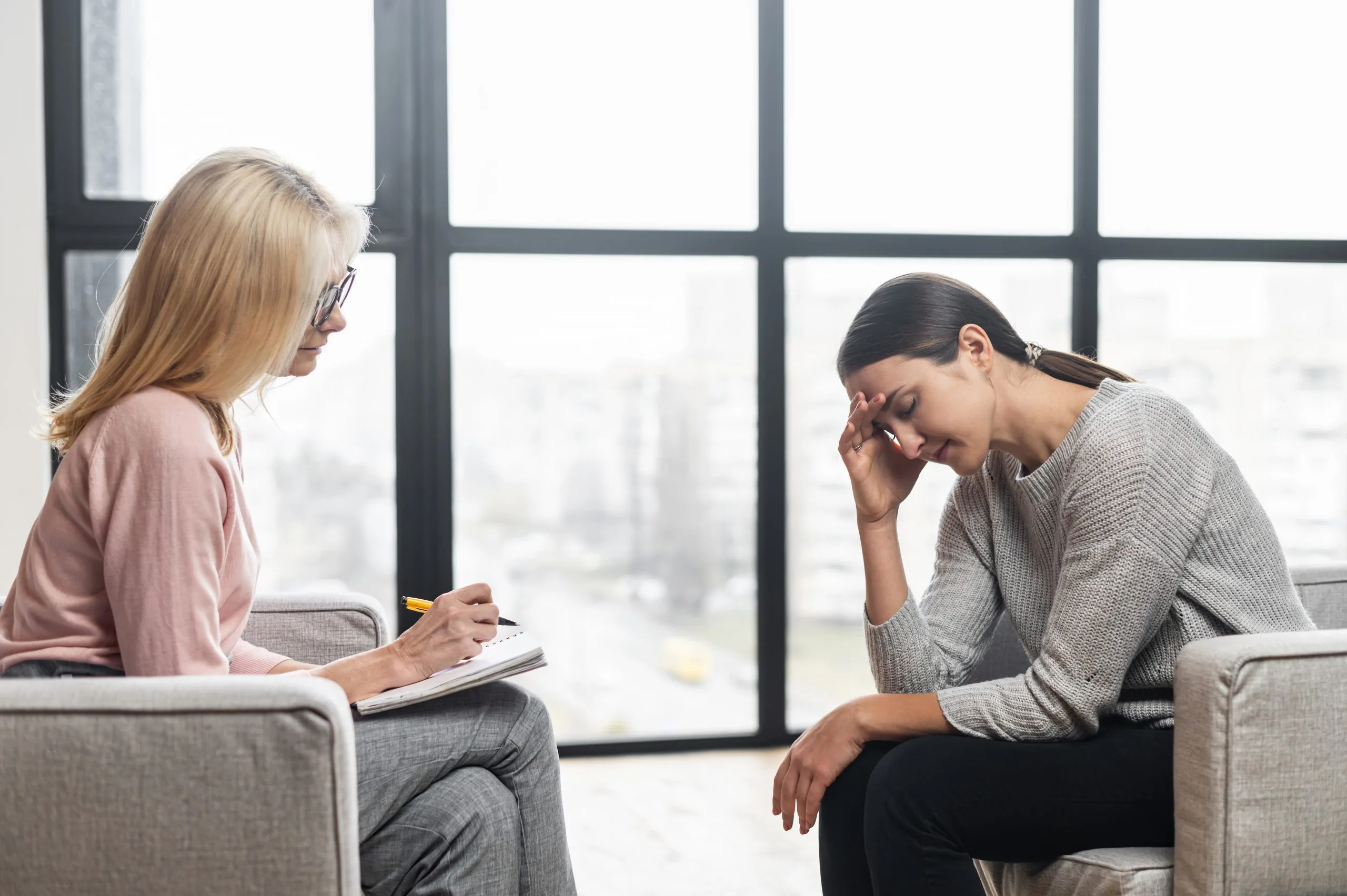 Woman in pink shirt taking notes while counseling distressed woman in gray sweater