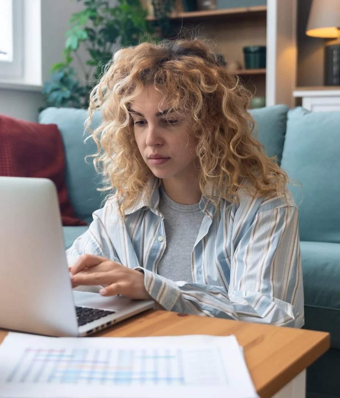 Woman with curly blonde hair looking concerned while using laptop on couch