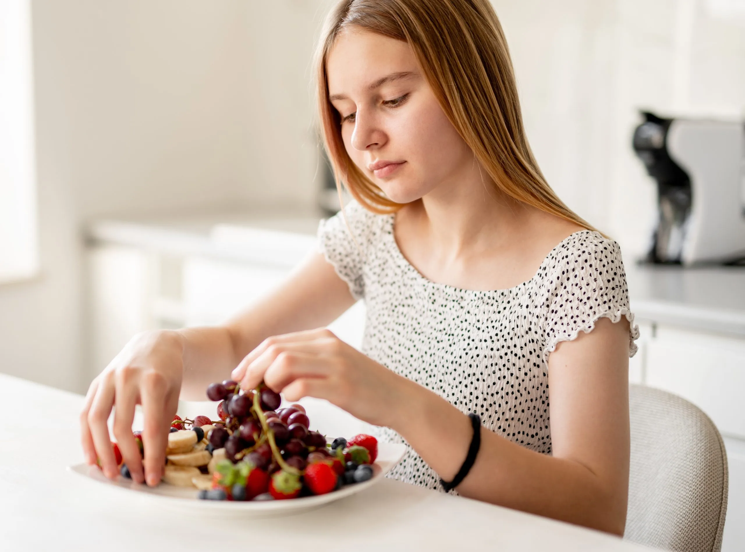 Girl reaching toward plate of fresh berries and pastries at kitchen table