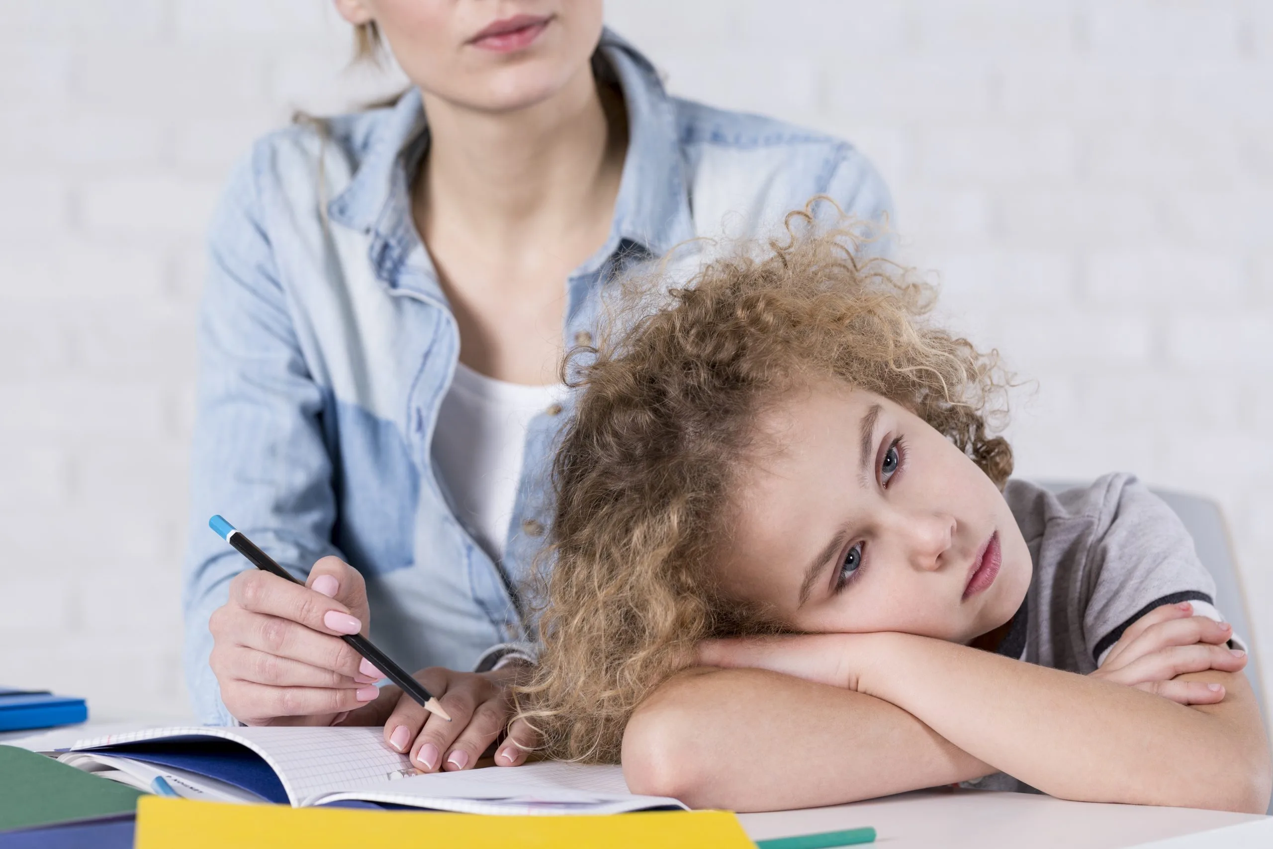 Woman helping child with homework at table with colorful books and writing materials