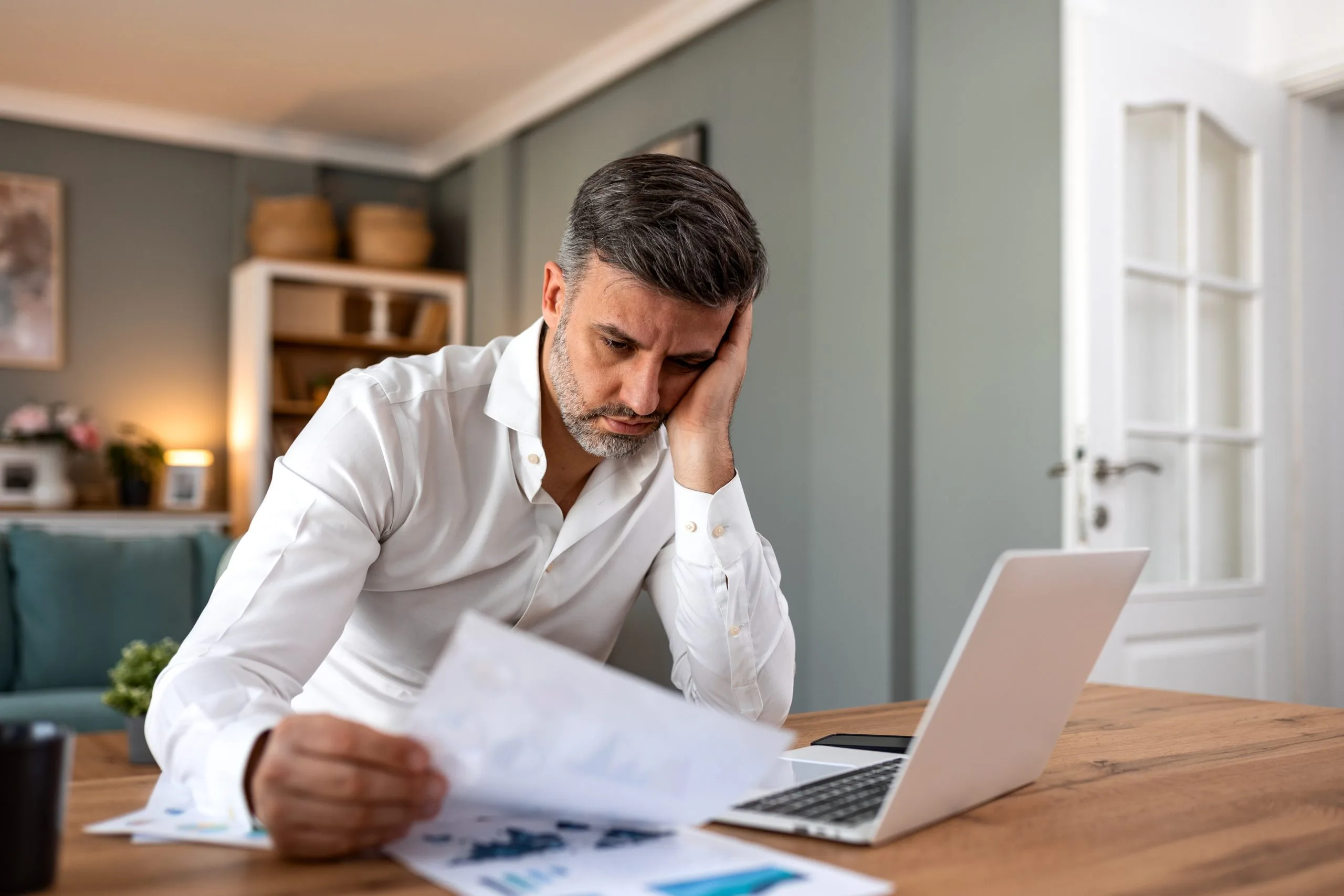 Stressed man at his desk holding his head while reading paperwork