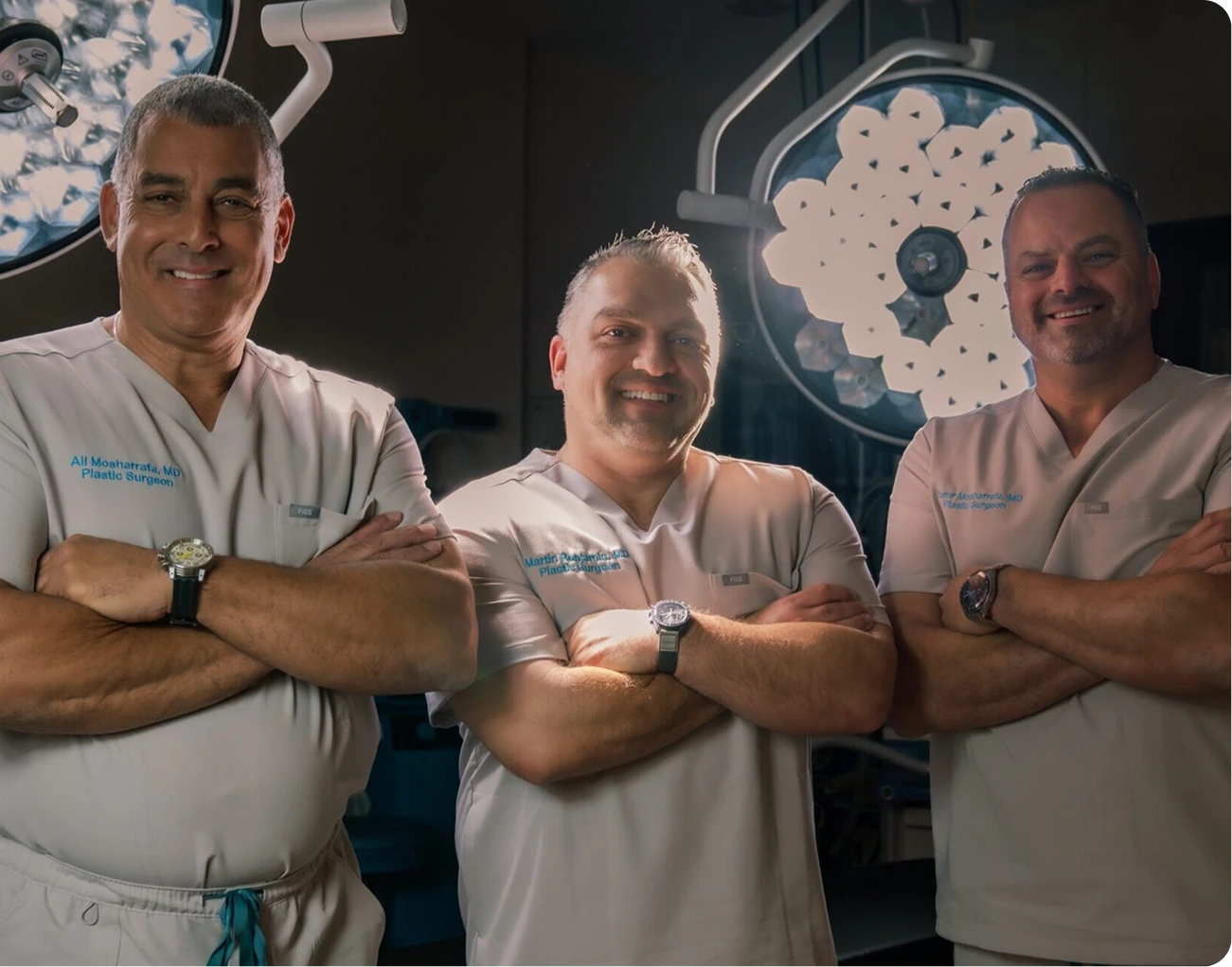 Ali Mosharrafa, MD and two plastic surgeons standing in an operating room with surgical lights above them
