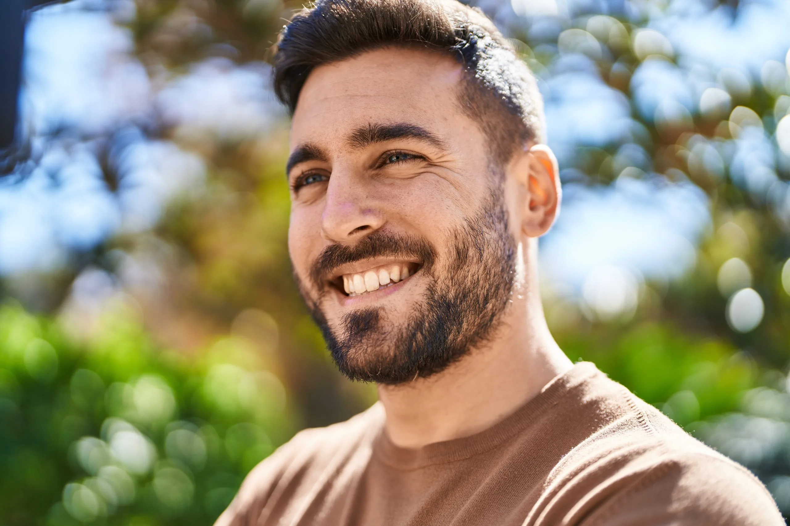 Smiling man with beard in outdoor setting with blurred green foliage background
