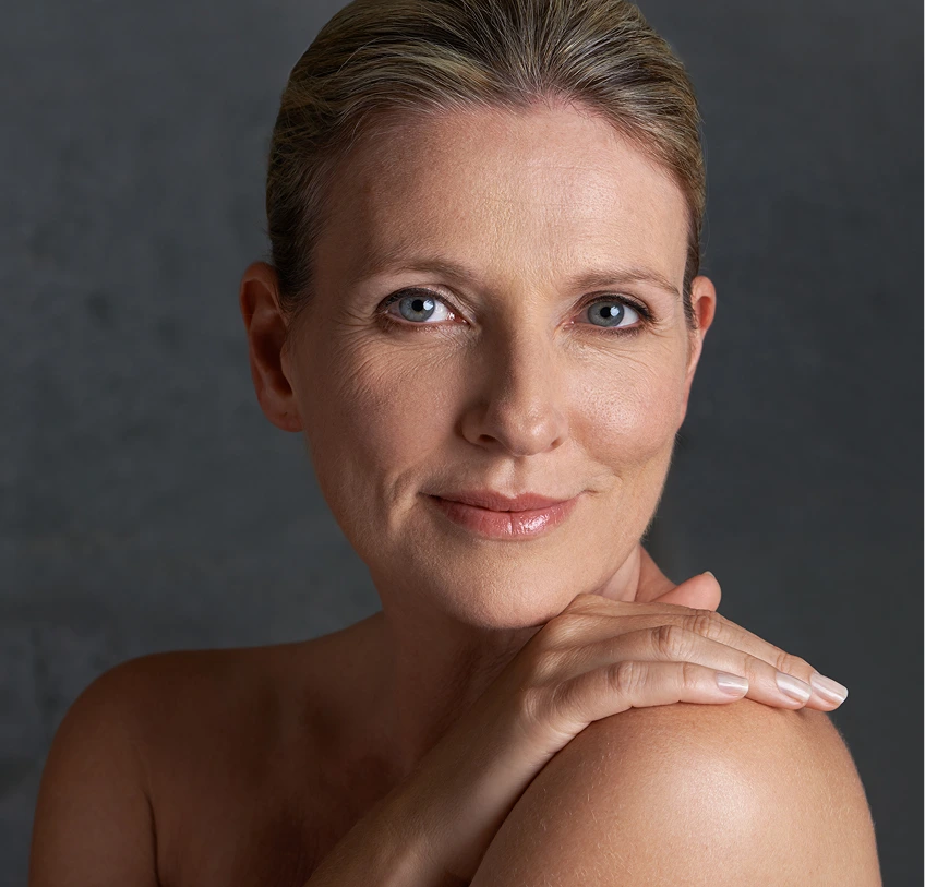 Woman with smooth, radiant skin smiling at camera with hand on shoulder