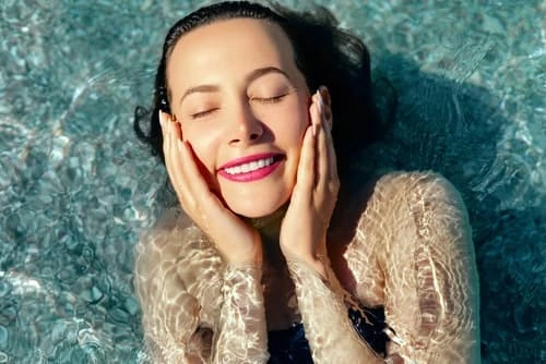 Woman with glowing skin touching her face against a textured teal background