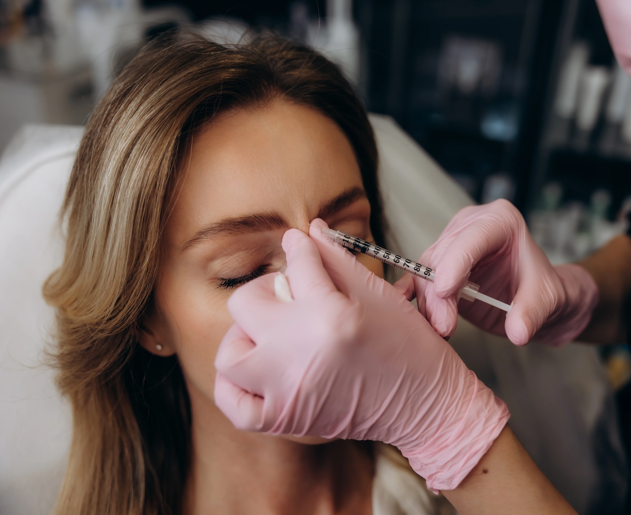 Clinician in pink gloves administering Botox injection to patient's forehead area
