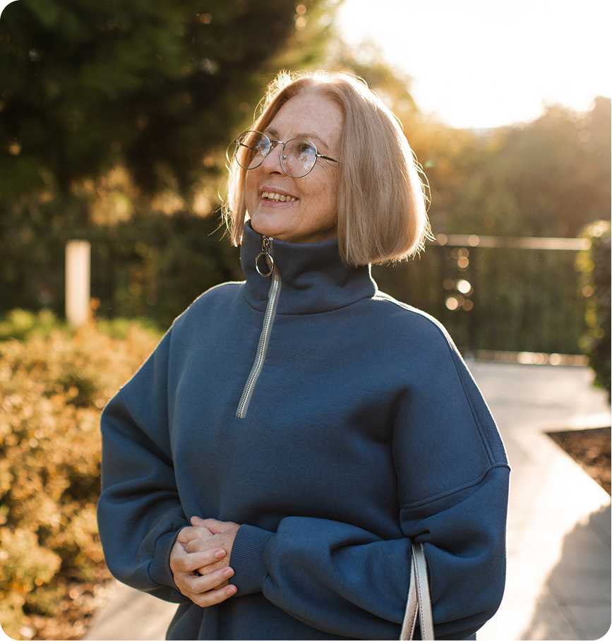 Woman wearing glasses and blue turtleneck smiling outdoors at golden hour