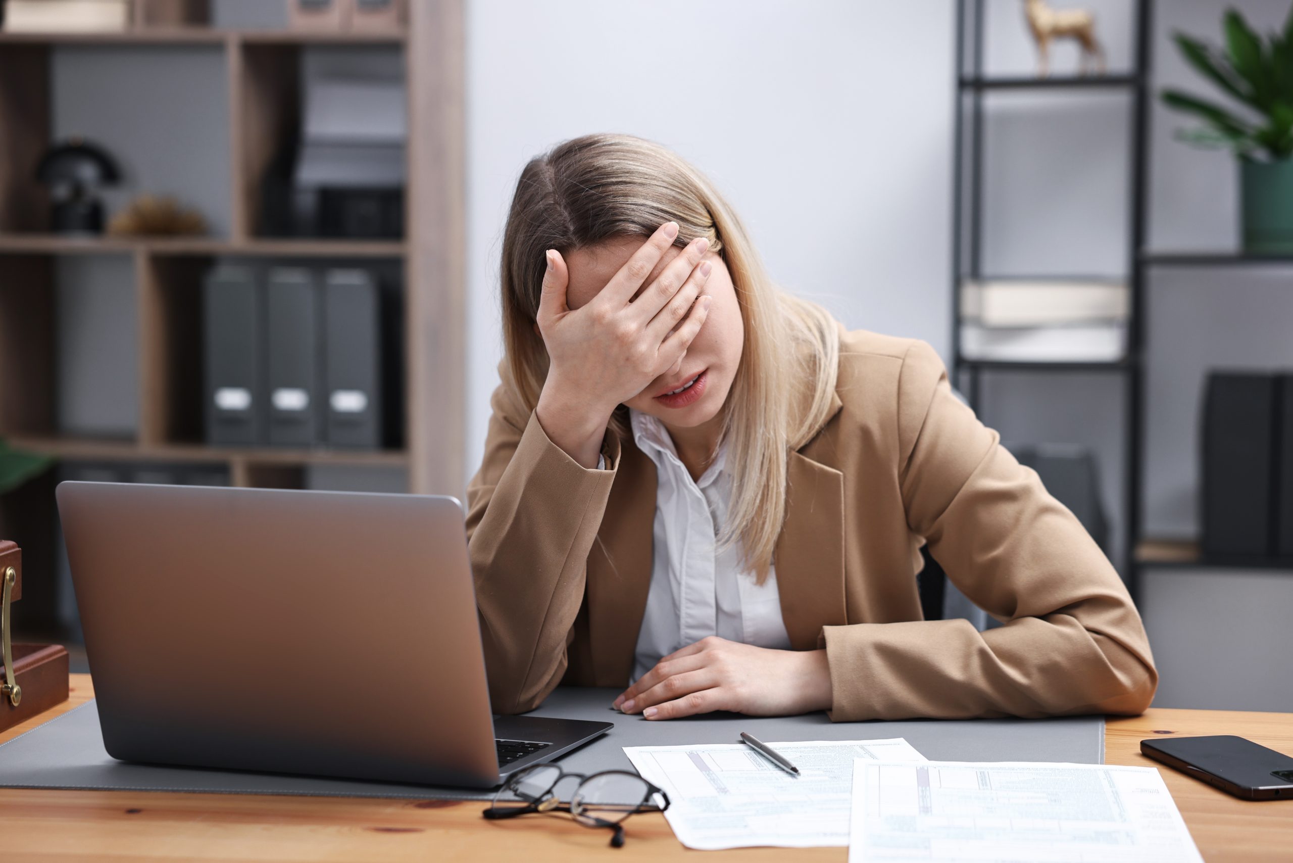 Woman at office desk holding her head in hand while looking at laptop, expressing stress and burnout