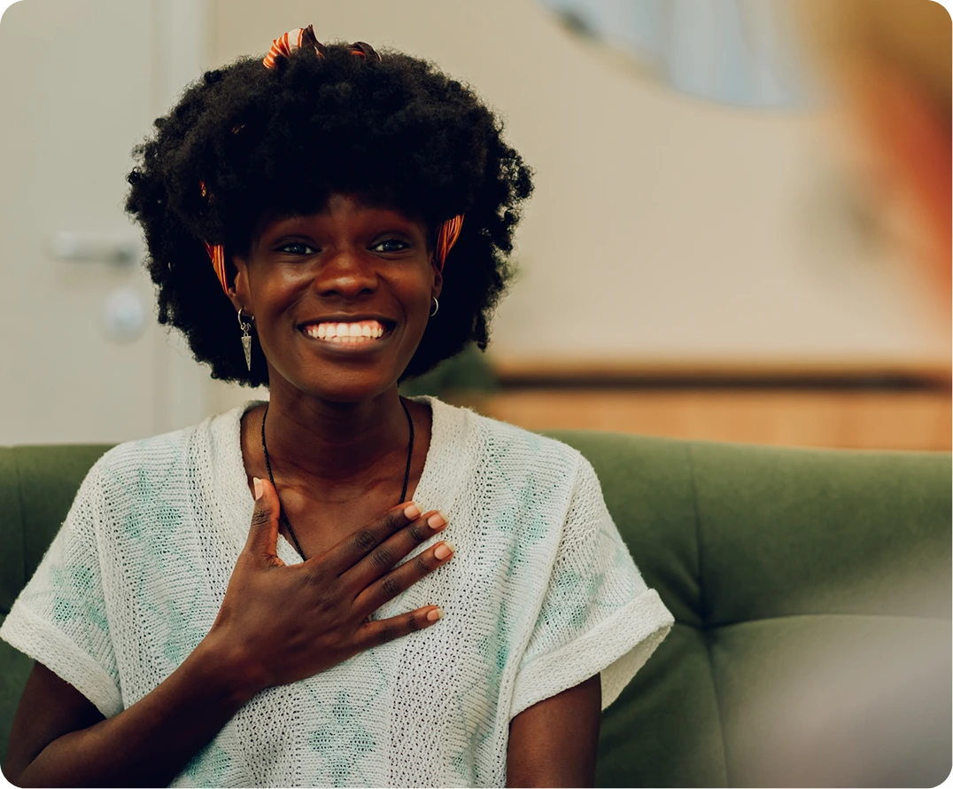 Woman smiling warmly with hand on chest, seated on green couch in therapy setting