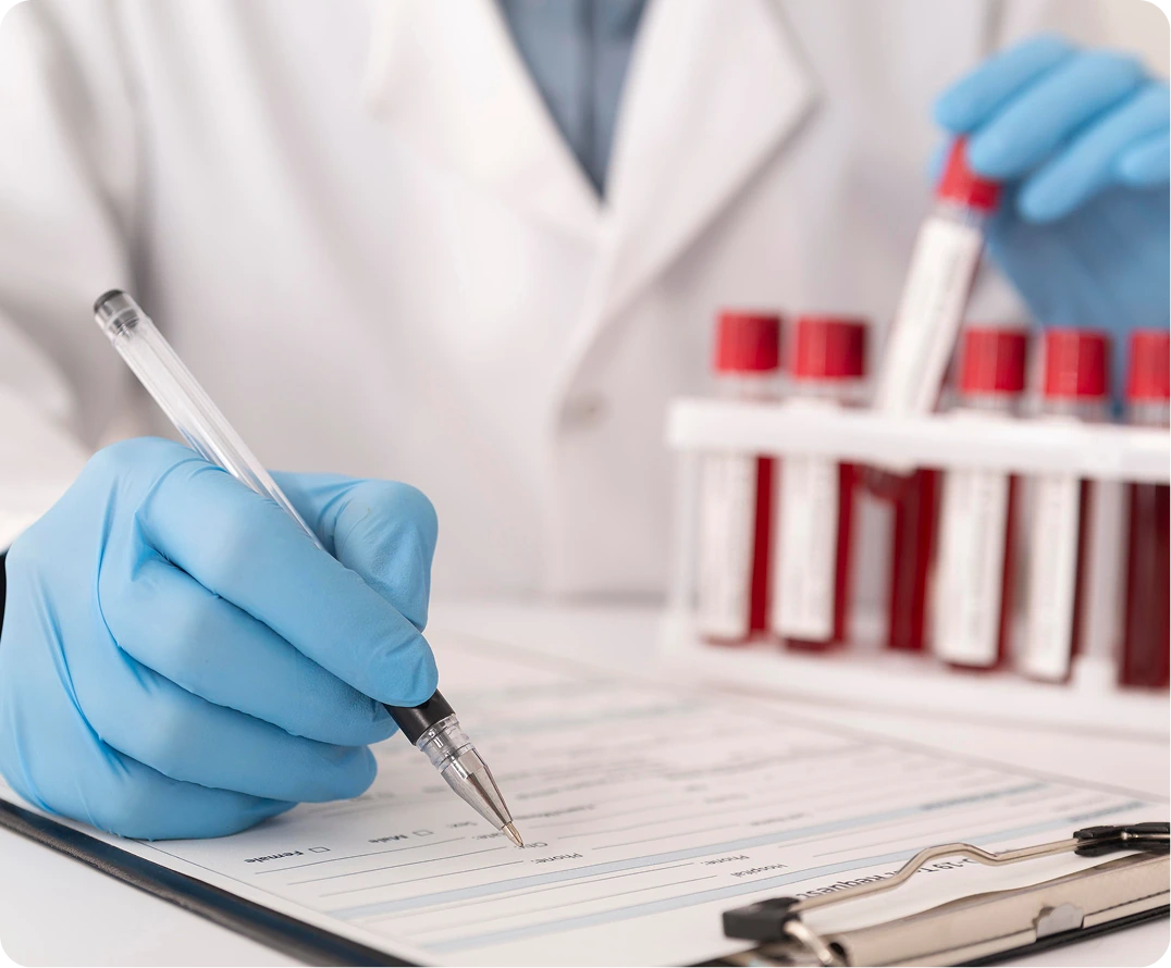 Healthcare provider in blue gloves documenting medication management notes while blood sample vials sit in the background