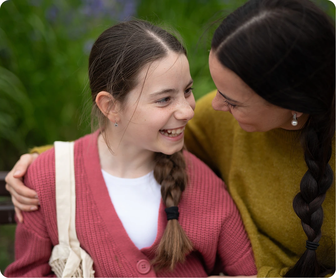 Adult and young teen smiling together outdoors with green foliage background
