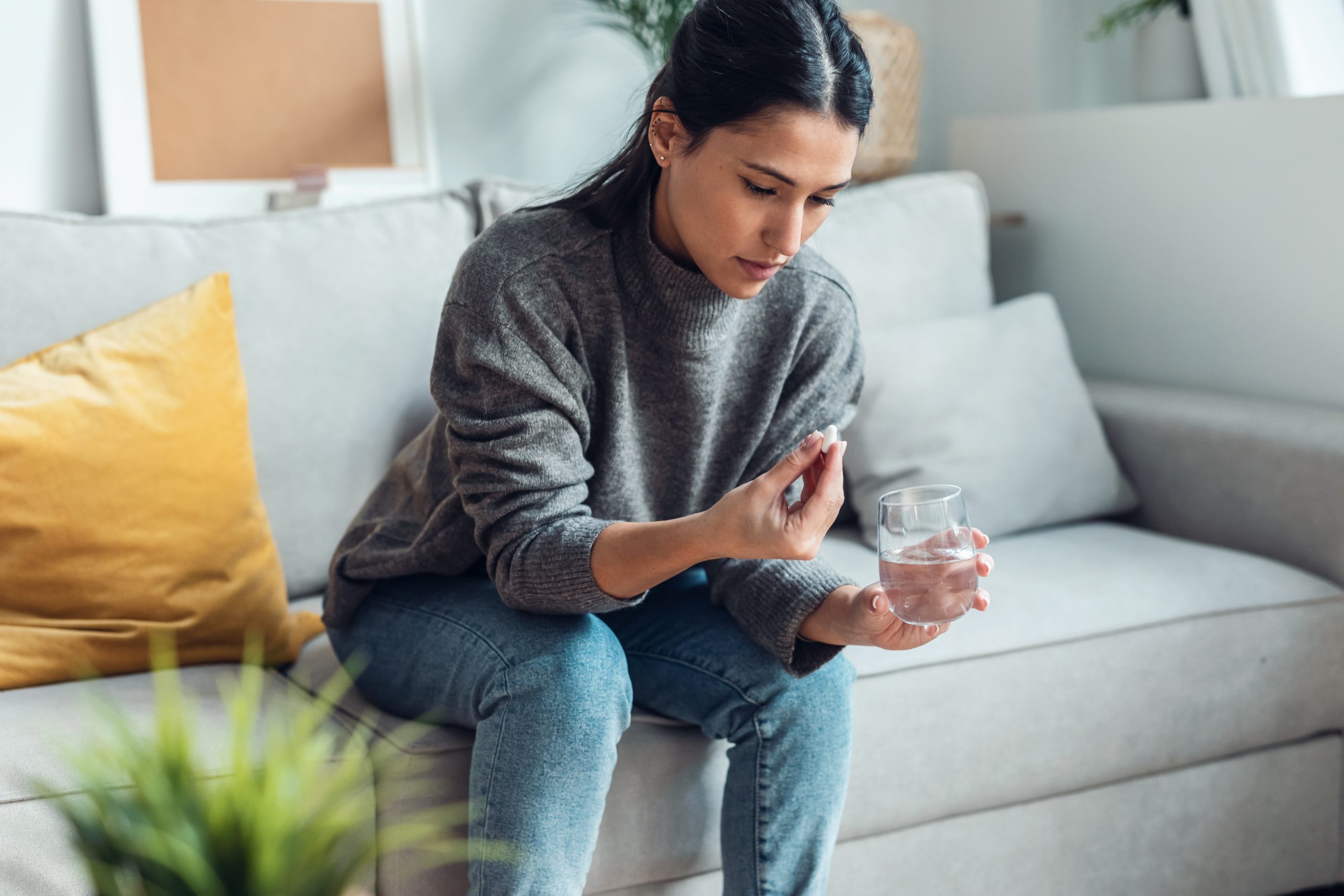 Woman sitting on couch taking a pill with a glass of water