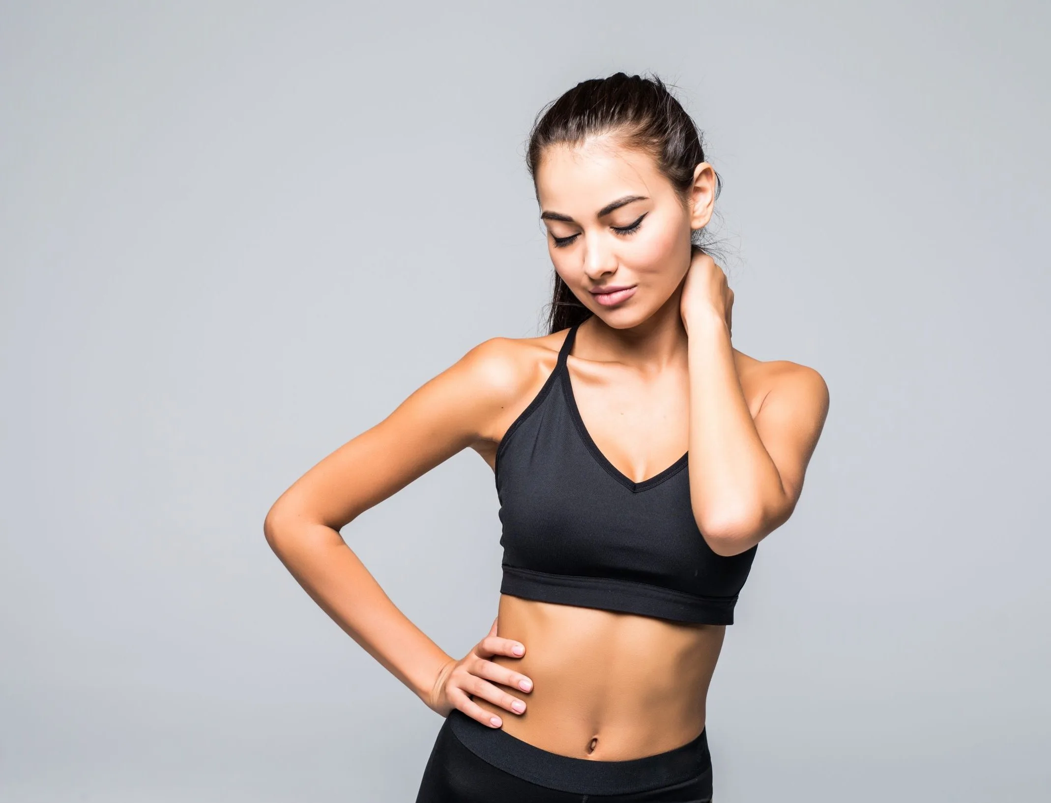 Athletic woman in black sports bra touching her neck, illustrating fatigue and muscle strain