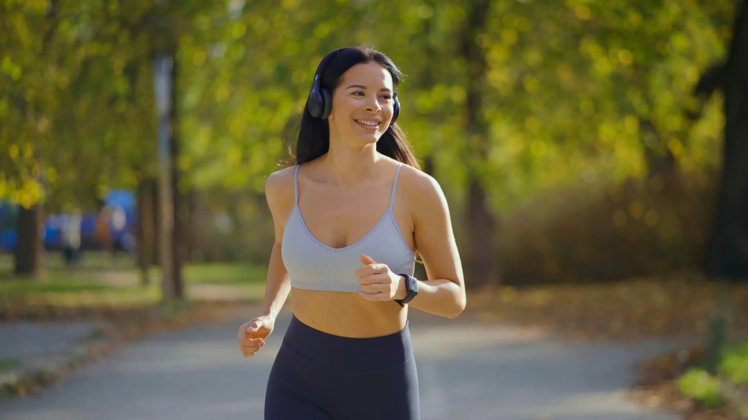 Woman jogging outdoors on a tree-lined path wearing headphones and athletic wear