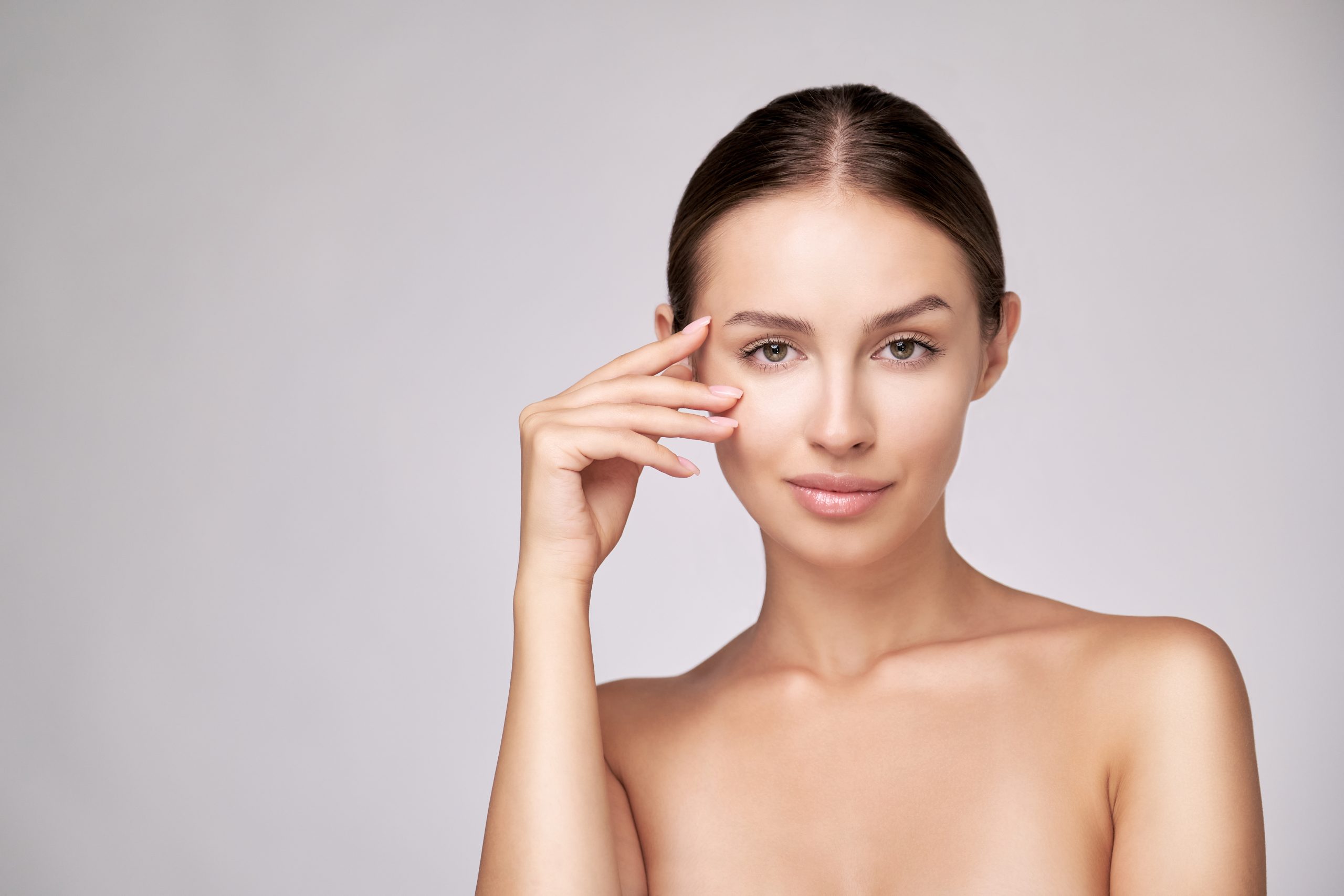 Woman touching under her eye with concerned expression against neutral background