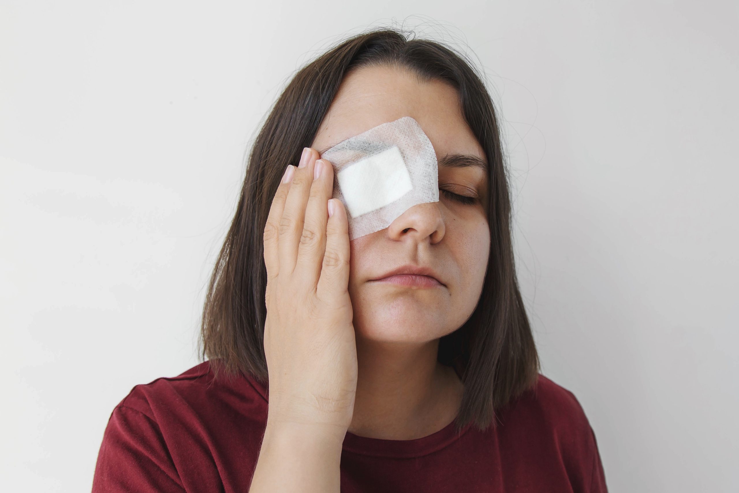 Woman holding gauze patch over eye during post-procedure recovery