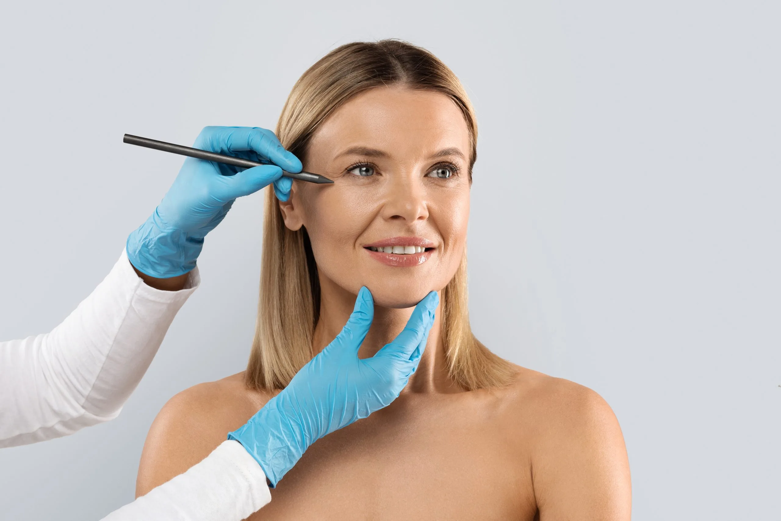 Practitioner marking woman's face with surgical pen while wearing blue gloves