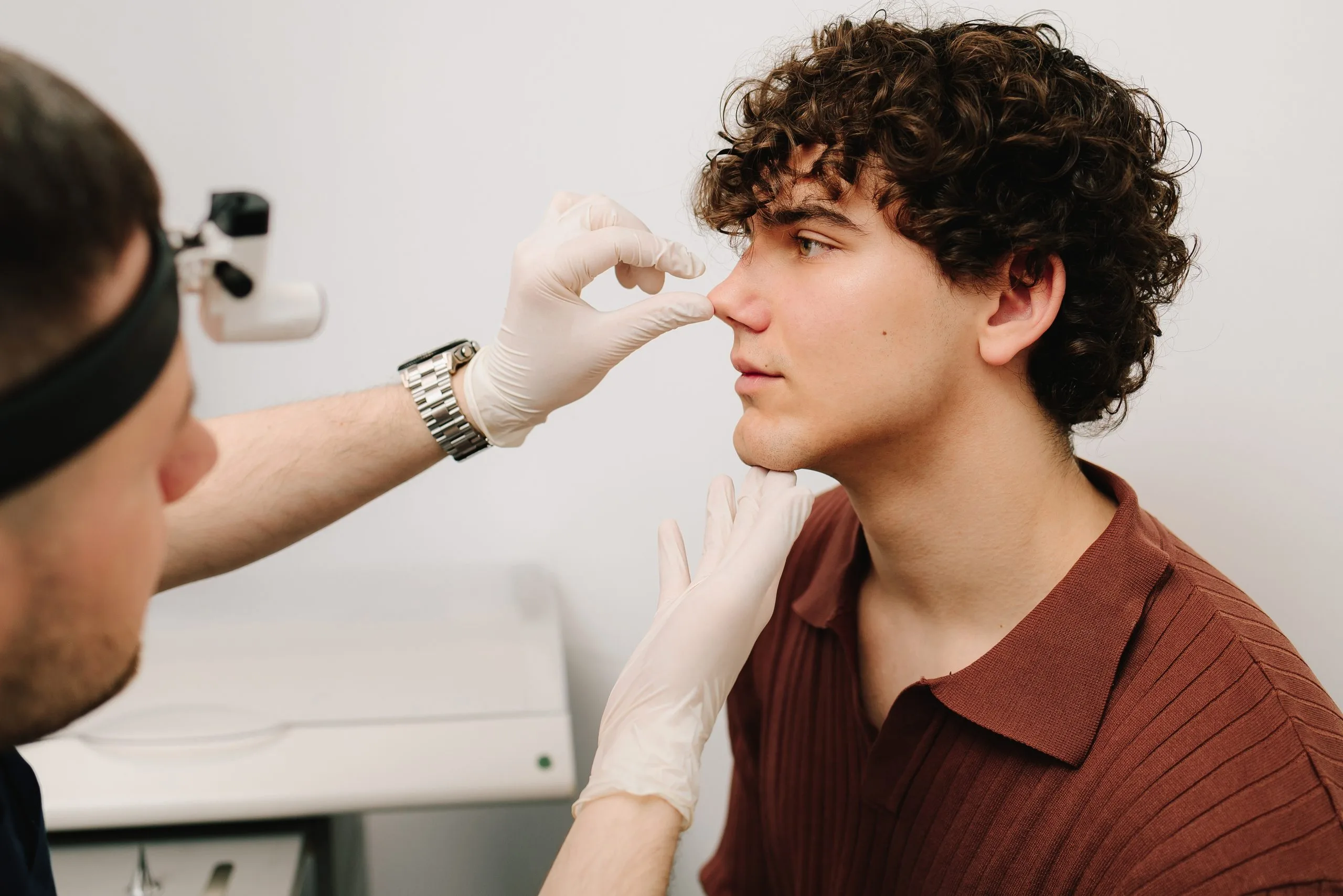 Practitioner examining young man's nose with magnification device