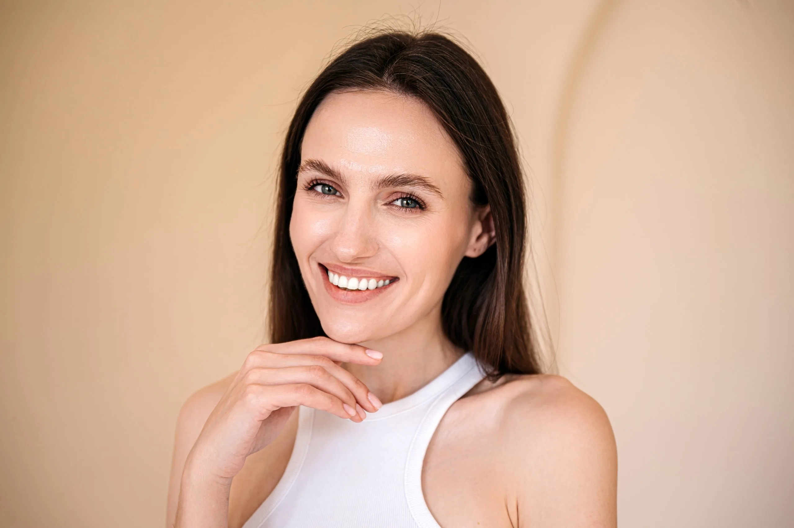 Woman with long dark hair smiling at camera against neutral beige background