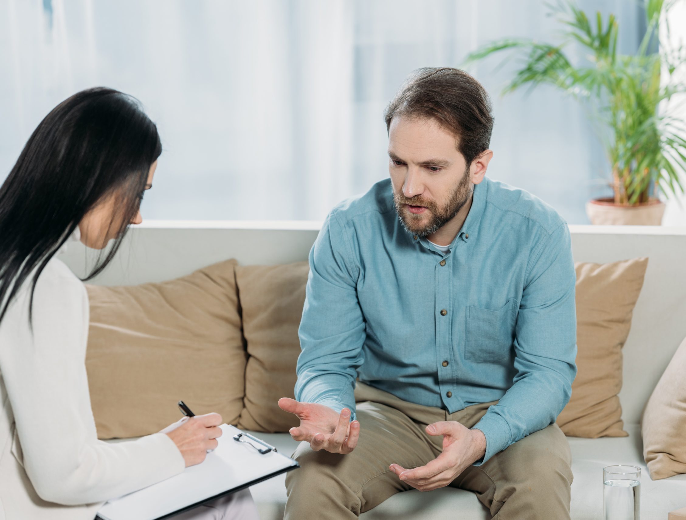 Therapist taking notes while man in blue shirt discusses concerns during counseling session