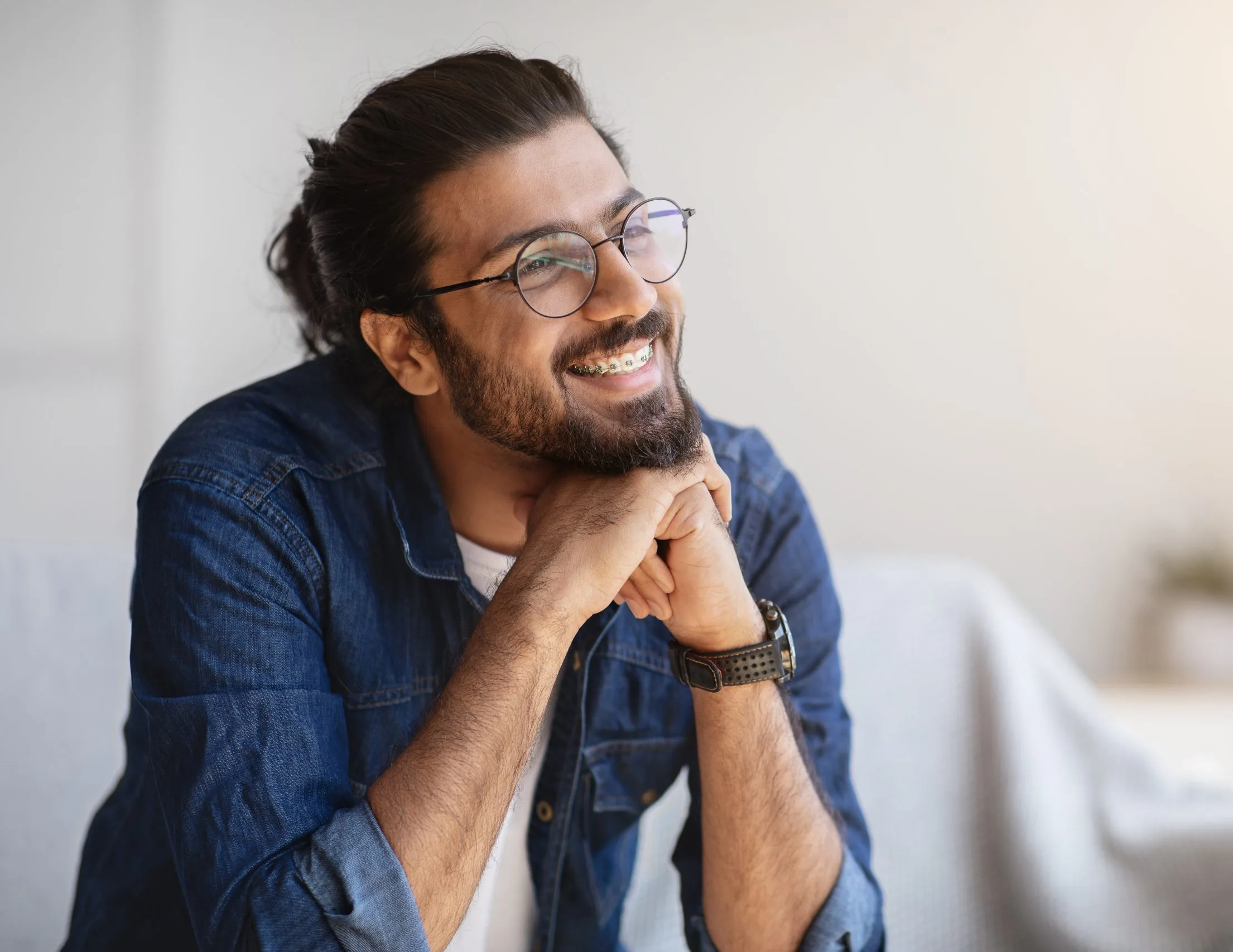Man with glasses smiling contentedly while resting chin on hands