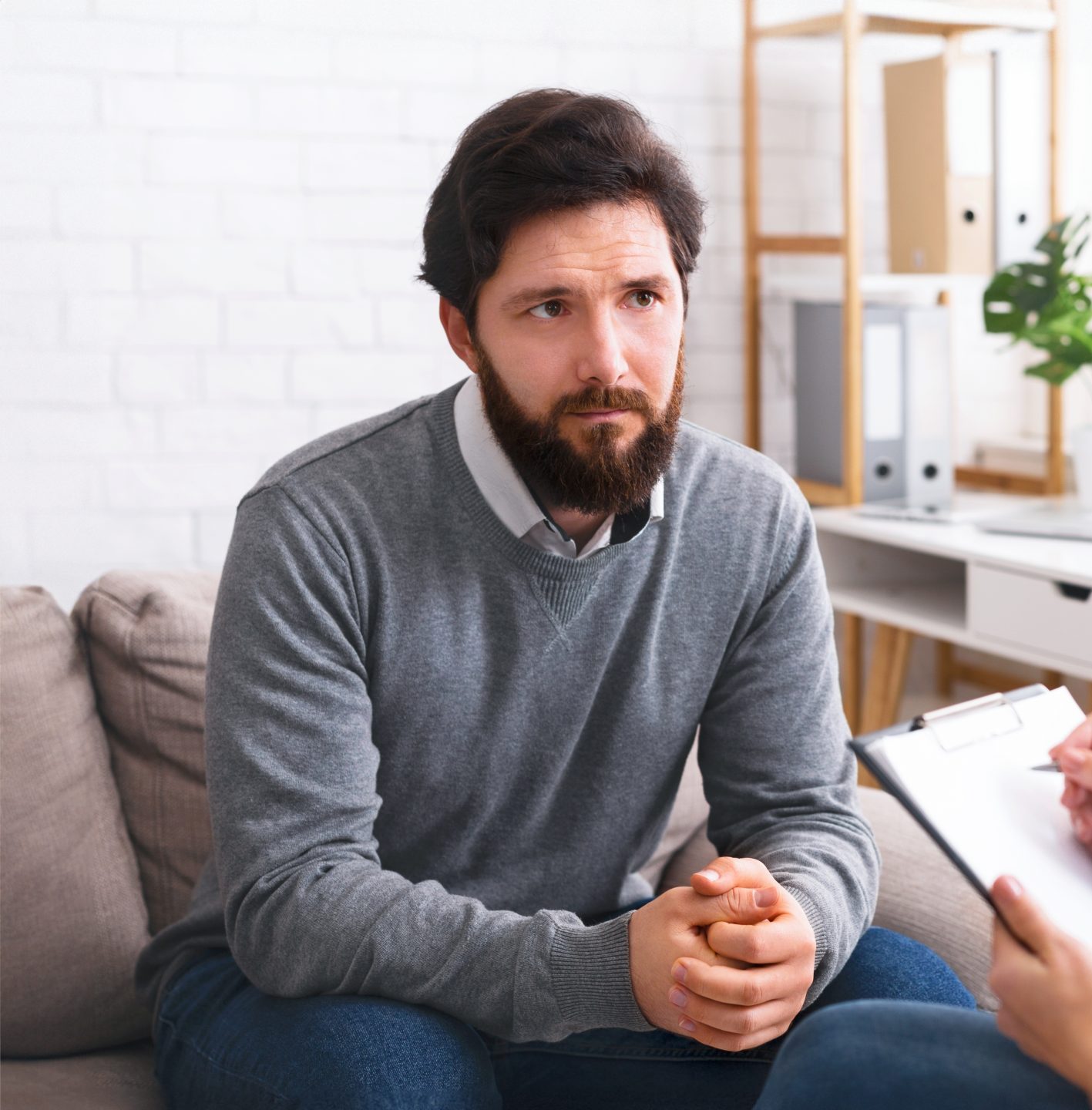 Male patient sitting on couch looking concerned during counseling session with therapist