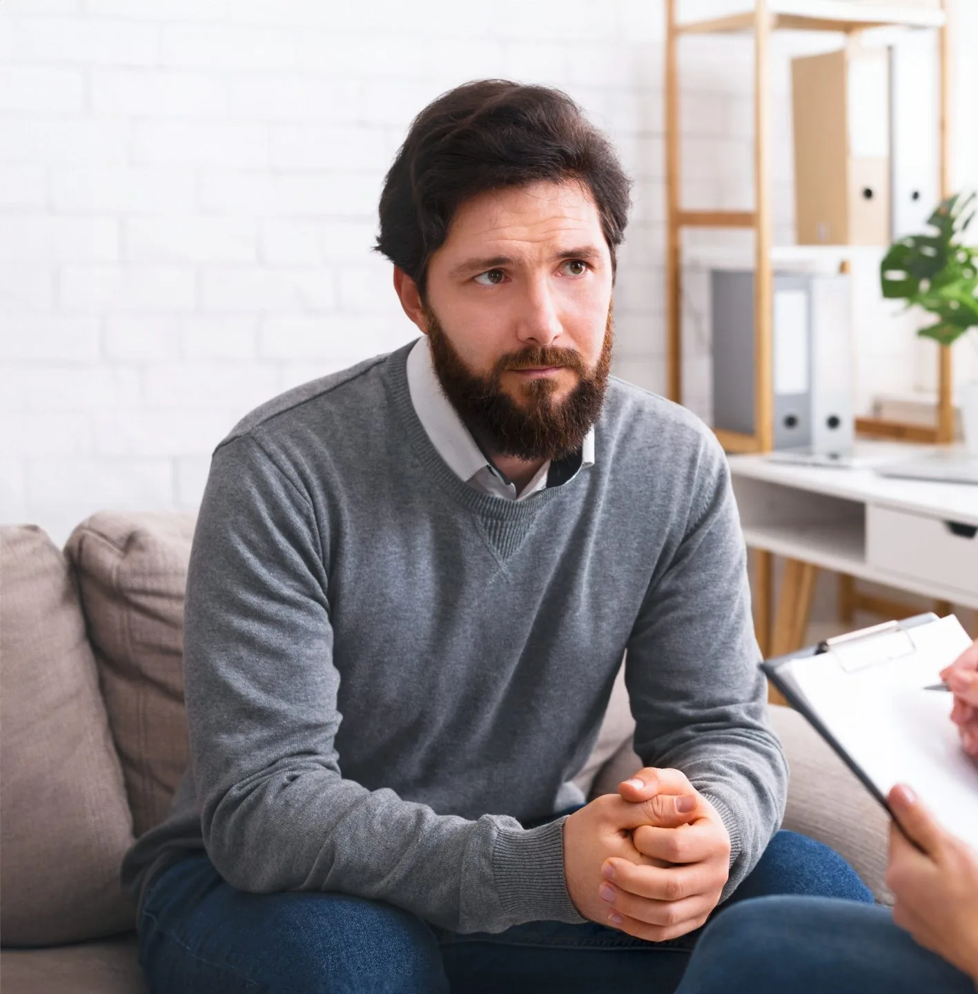 Male patient sitting on couch looking concerned during counseling session with therapist