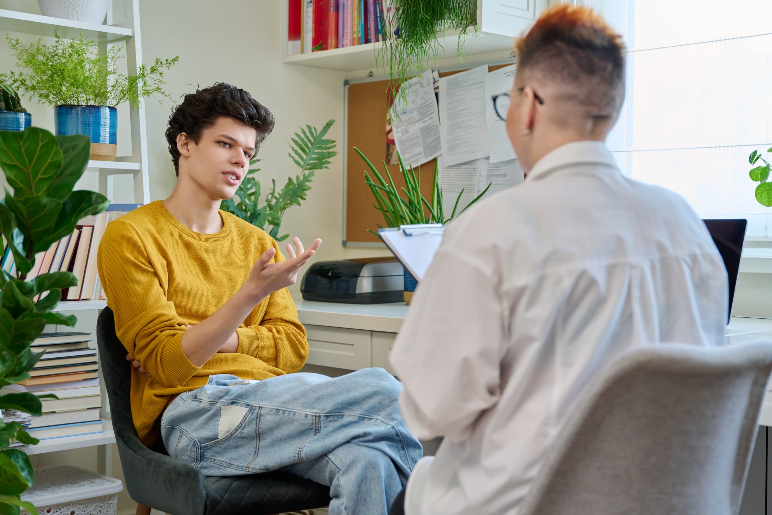 Man in yellow shirt speaking with therapist in plant-filled office setting