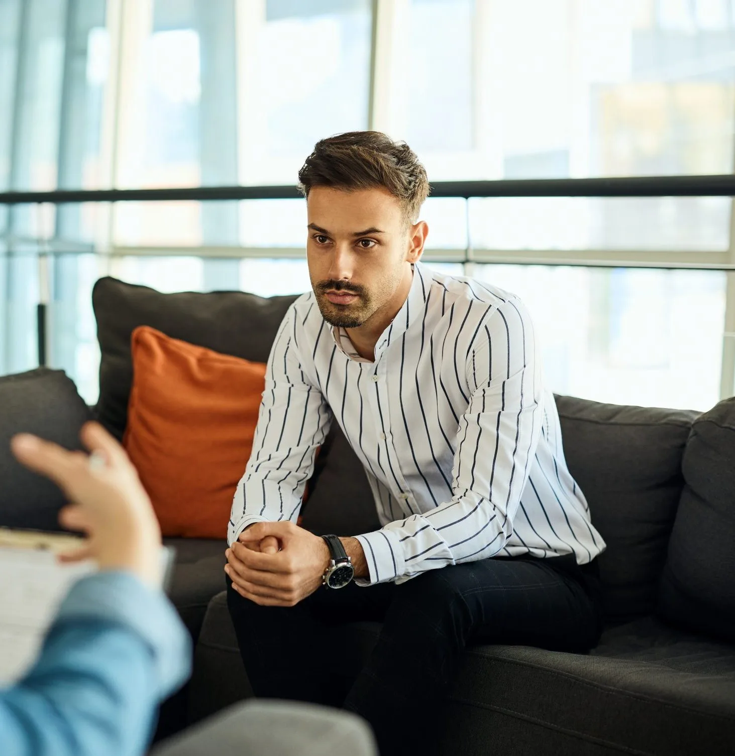 Man in striped shirt listening attentively during conversation in modern office with city view