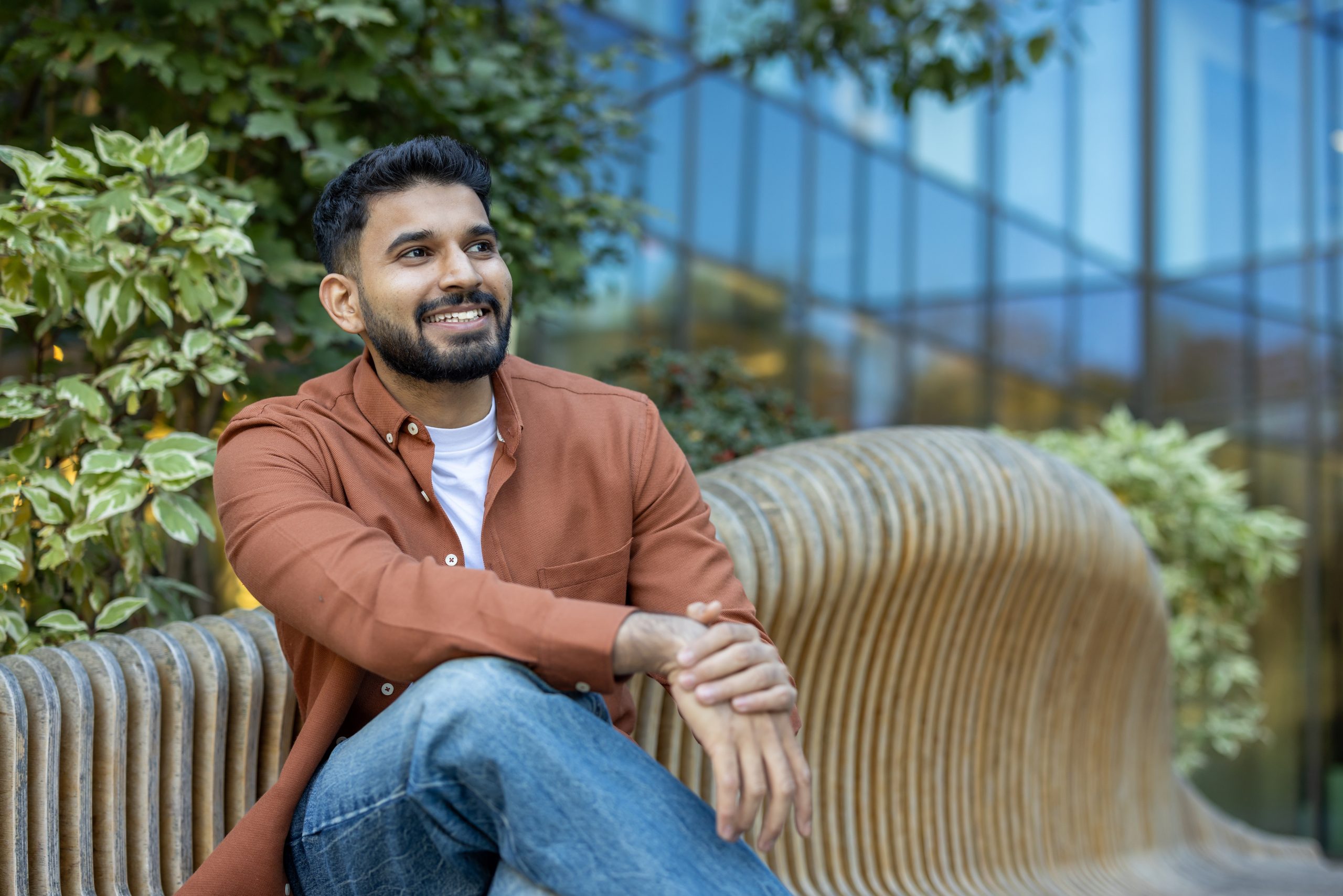 Man smiling while sitting on a striped chair outdoors surrounded by plants