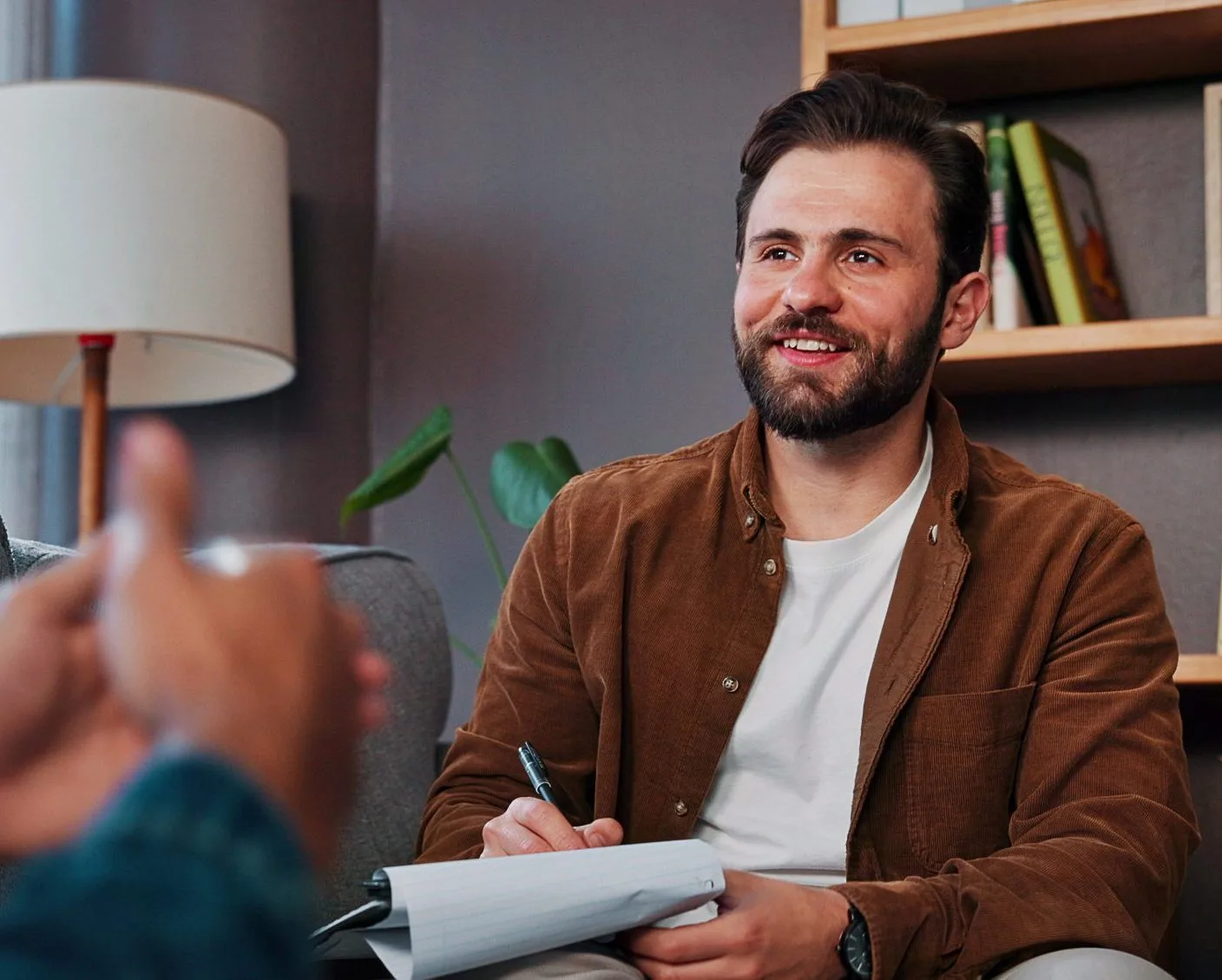 Man smiling while writing notes during therapy or coaching session