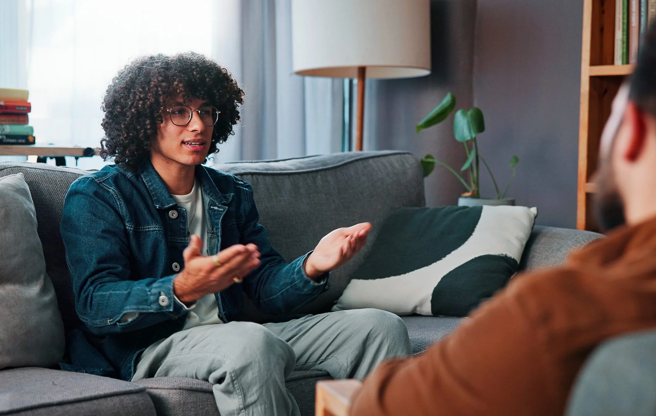 Young man on couch gesturing while discussing with therapist in modern office setting