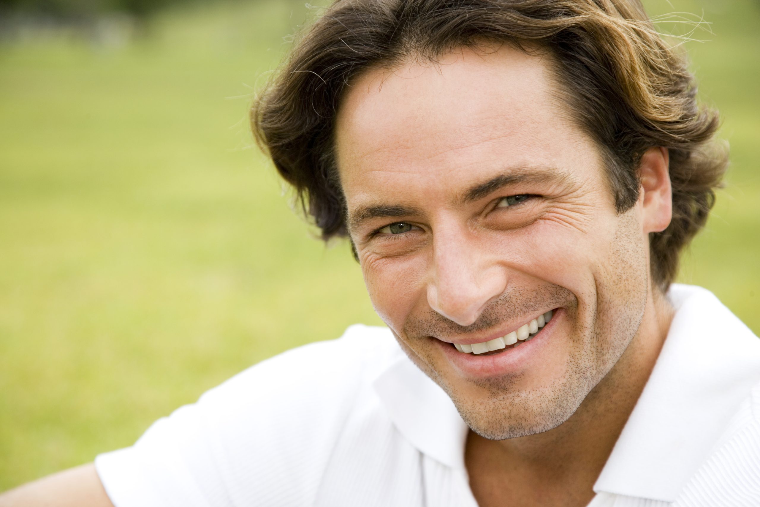 Man smiling outdoors in white shirt against a blurred green background