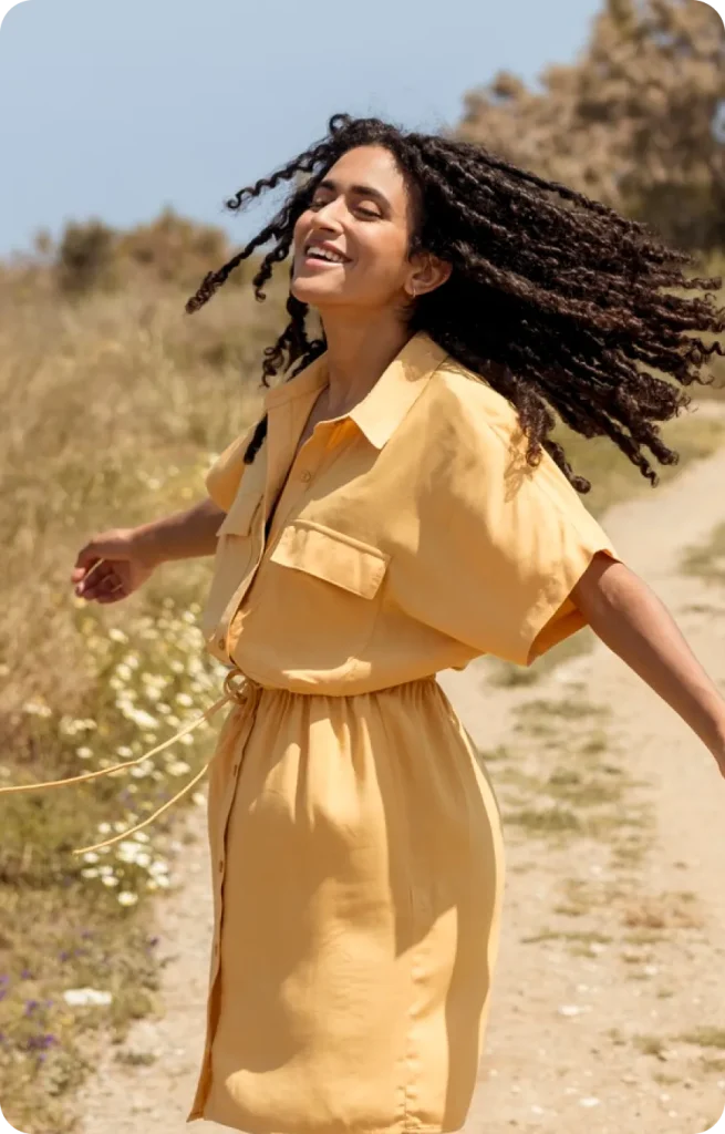 Woman in yellow dress smiling outdoors on a desert trail with wildflowers and rock formations