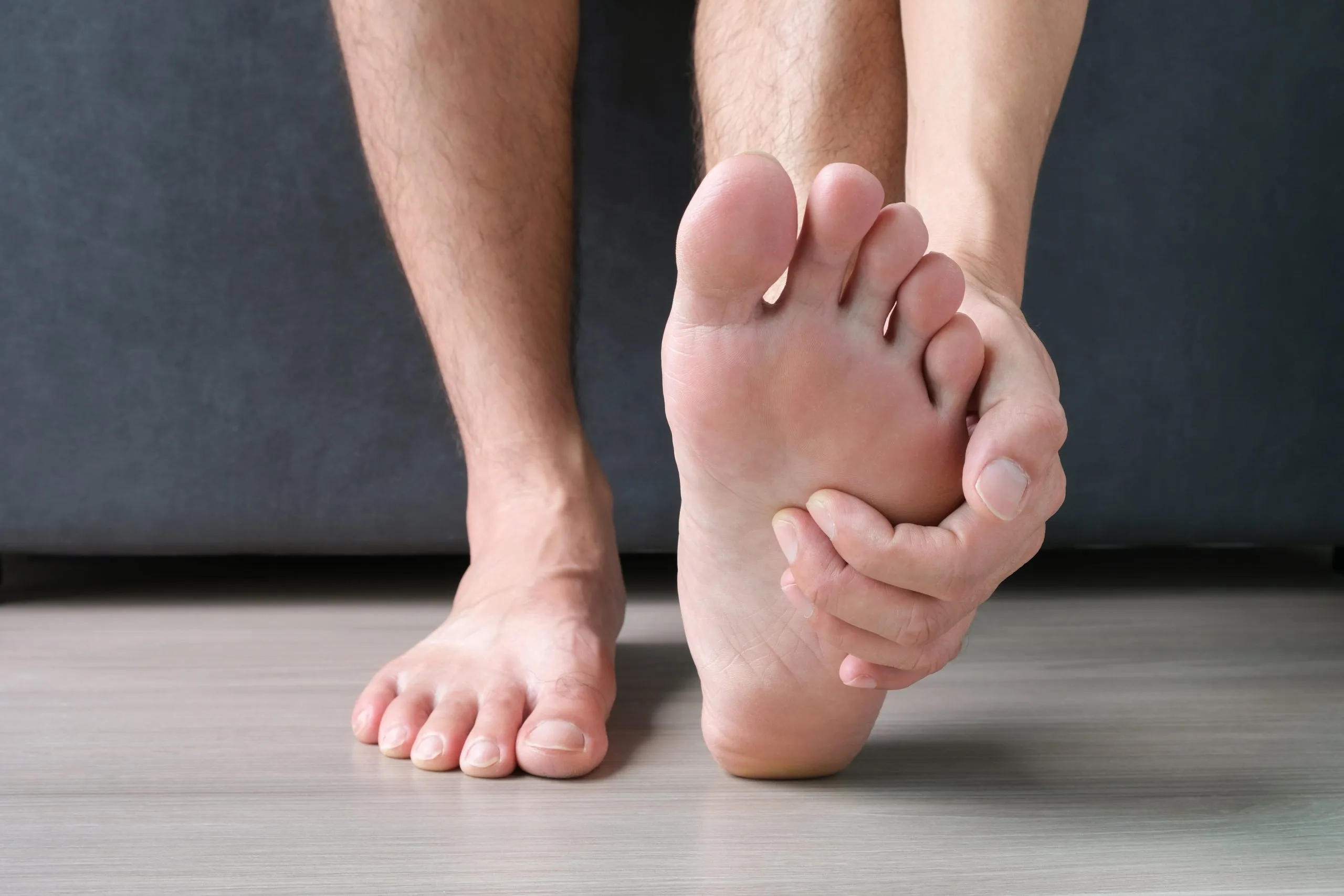 Man sitting on floor holding his foot, showing foot and ankle pain