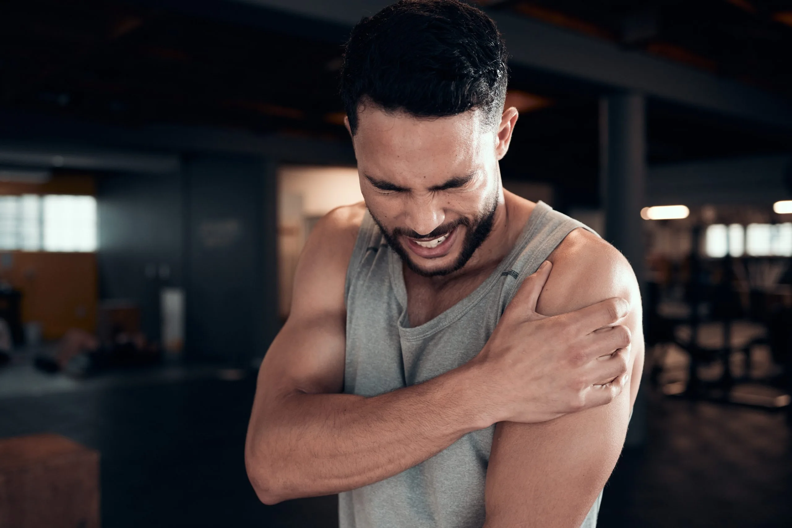 Man at gym holding his shoulder with expression of shoulder pain