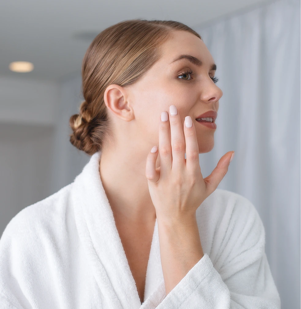 Woman in white robe touching her face indoors