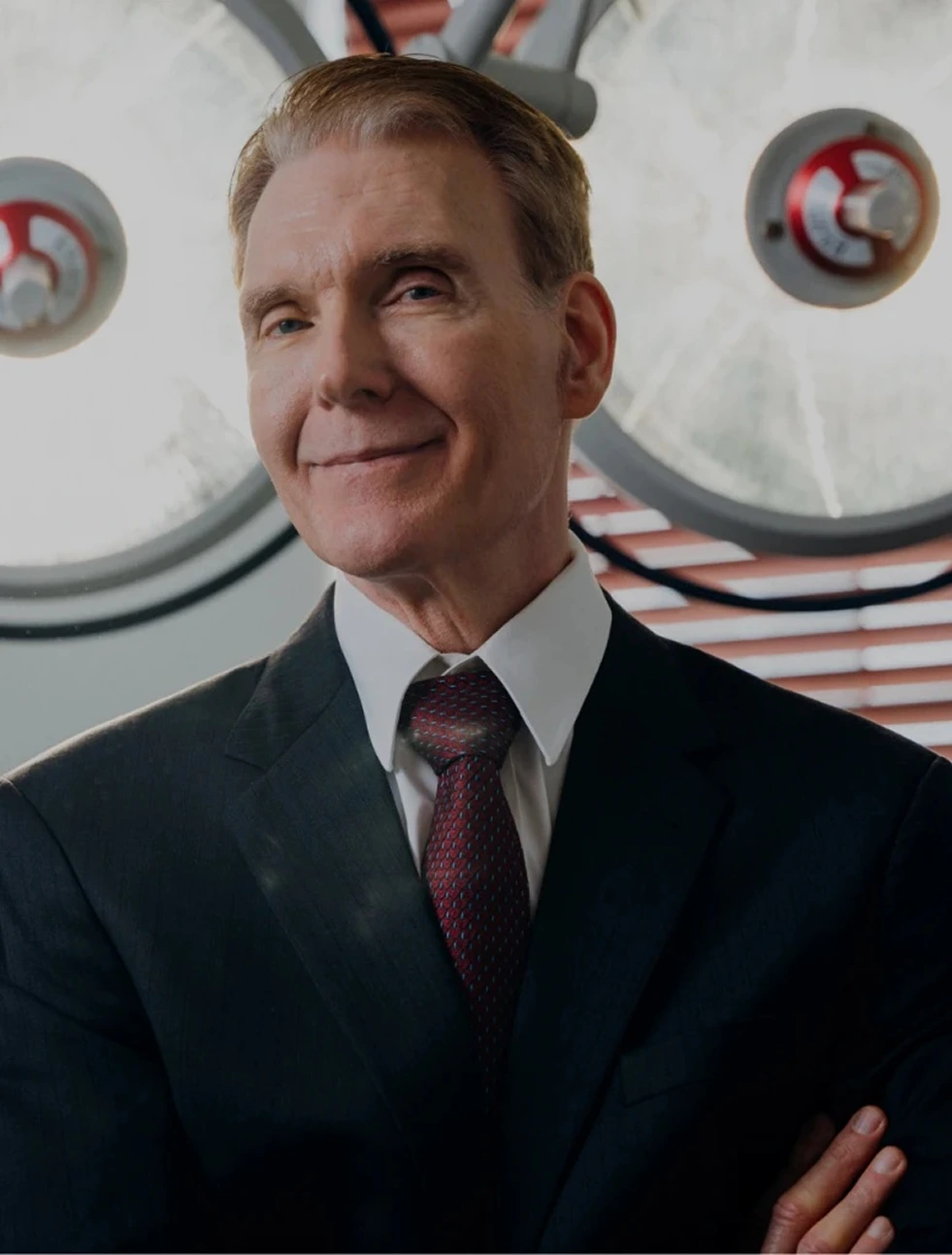 Plastic surgeon in dark suit and burgundy tie standing in front of surgical lights