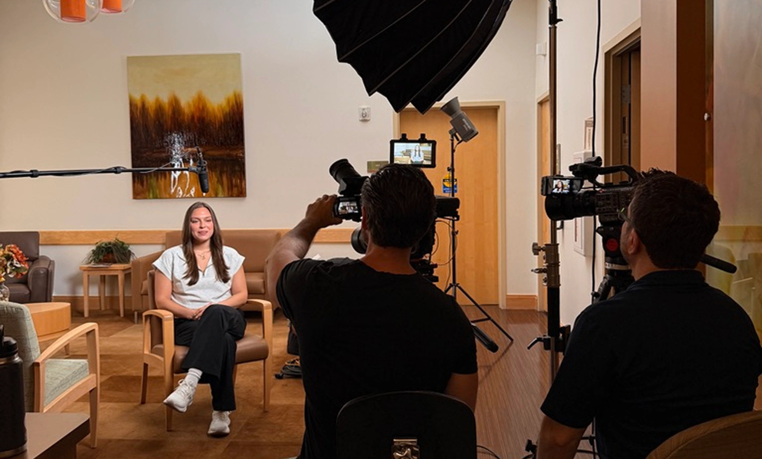 Videographer filming a woman seated in a modern office lounge during a professional shoot
