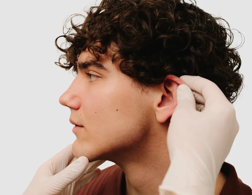 Surgeon's hands examining patient's ear during otoplasty assessment